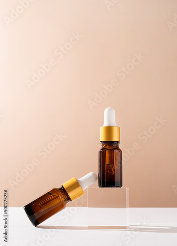Amber glass dropper bottles with a pippette with white rubber tip on glass podium and beige background, mockup design photo
