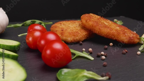 Slow rotating cinematic close up shot of perfectly cooked golden brown schnitzel on a slate platter with garnish of tomatoes, arugula, cucumber, garlic and peppercorns, cut out photo