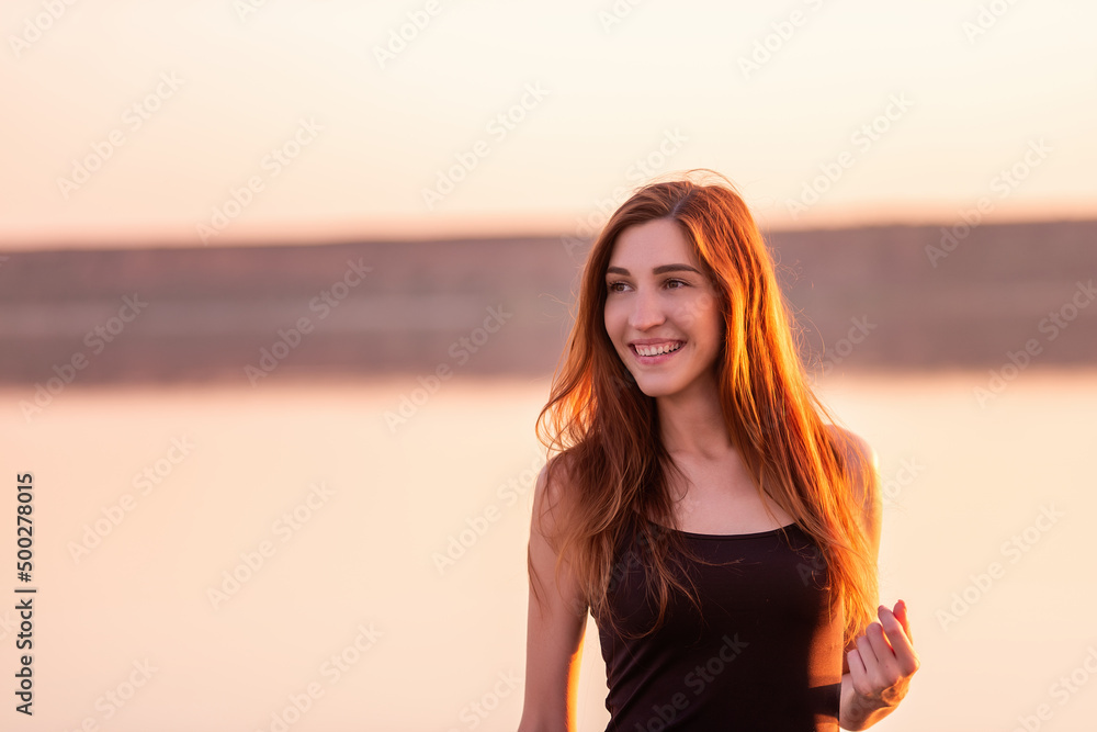 Close-up portrait of young woman in black dress against the sunset sky. Woman walks on the seashore