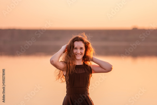 Close-up portrait of curly, happy dancer in airy black dress at sunset. Young woman in the water © farmuty