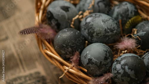 Easter card with a copy of the place for the text. Purple, blue eggs in a basket on a dark newspaper background. Natural dye karkade tea.