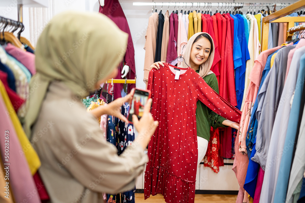 muslim woman taking picture of her friend while trying new clothes while shopping at the mall