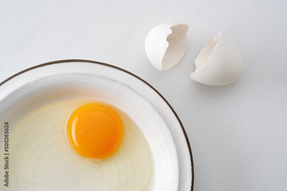 White egg broken egg with a yolk in a white plate. Cracked egg, eggshells with yolk on white background. Shallow depth of field White egg broken egg with a yolk in a white plate. Cracked egg, eggshells with yolk on white background. Shallow depth of field