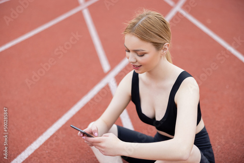 smiling sportswoman using mobile phone while sitting on stadium.