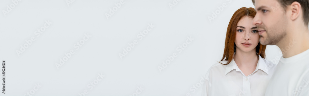 Red haired woman looking at camera near blurred boyfriend isolated on white, banner. Red haired woman looking at camera near blurred boyfriend isolated on white, banner.