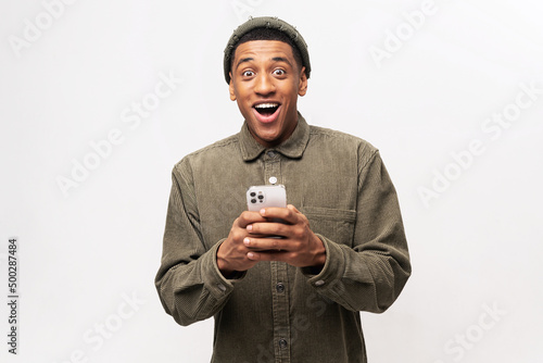 Funny surprised trendy guy suddenly read message on his mobile phone and expressing shock amazement, unbelievable news on smartphone. Studio shot isolated