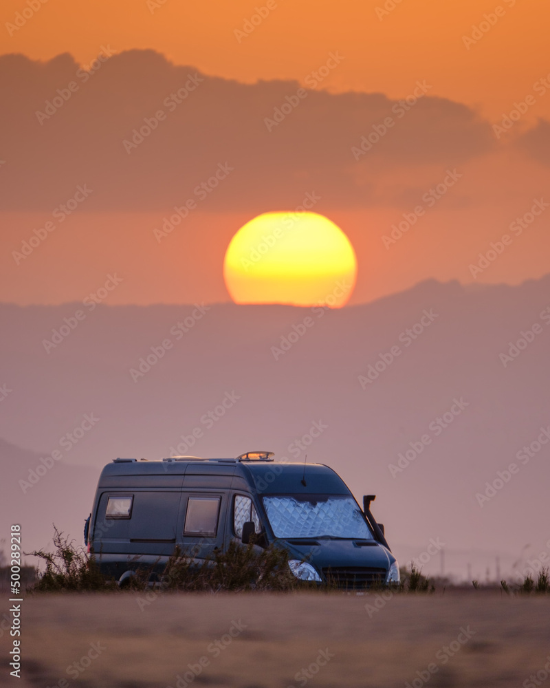 4x4 camper on the beach at sunset with a bright sun behind