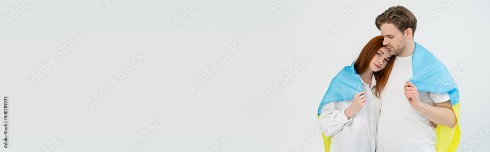 Young couple wrapped in ukrainian flag isolated on white, banner. Young couple wrapped in ukrainian flag isolated on white, banner.