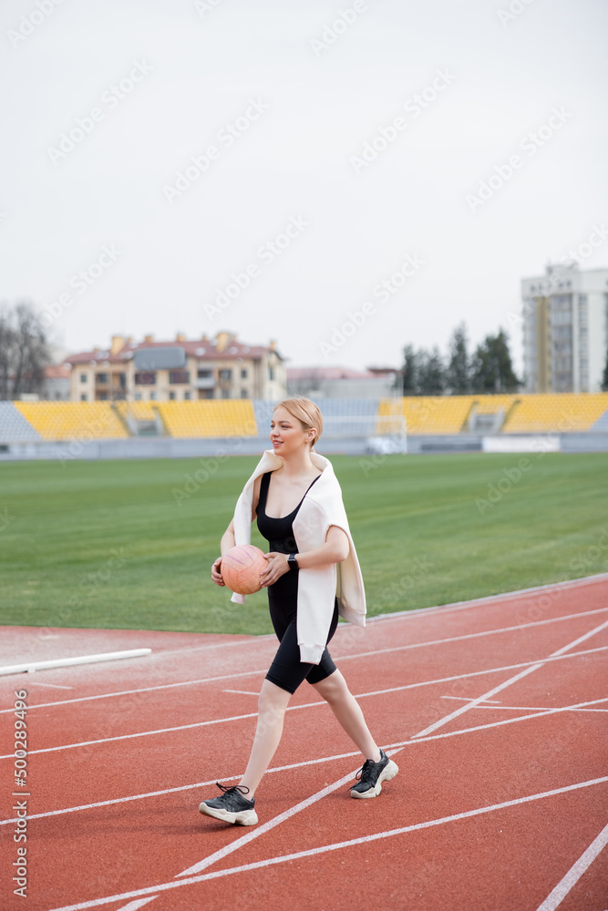 pleased woman in sportswear walking with ball on athletic field.