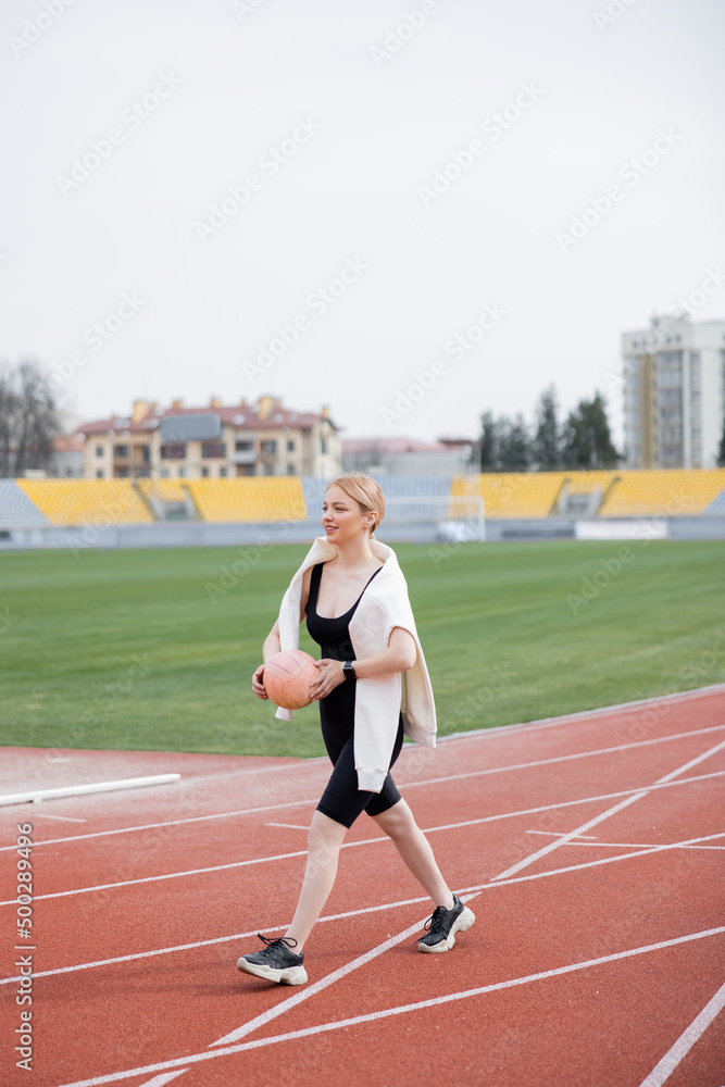 pleased woman in sportswear walking with ball on athletic field. pleased woman in sportswear walking with ball on athletic field.