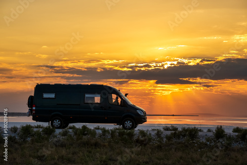 Backlit silhouette of a 4x4 camper van in a desert landscape at sunset © JoseMaria