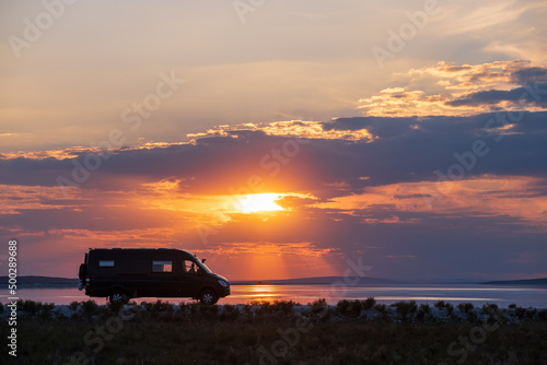 Backlighting silhouette of a camper next to a salt lake at sunset © JoseMaria