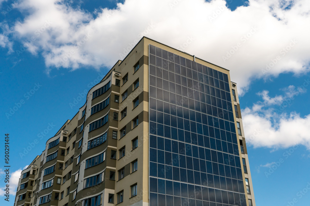 Movement of clouds against the background of a modern energy-efficient building. Multi-storey residential building with solar panels on the wall. Renewable energy in the city