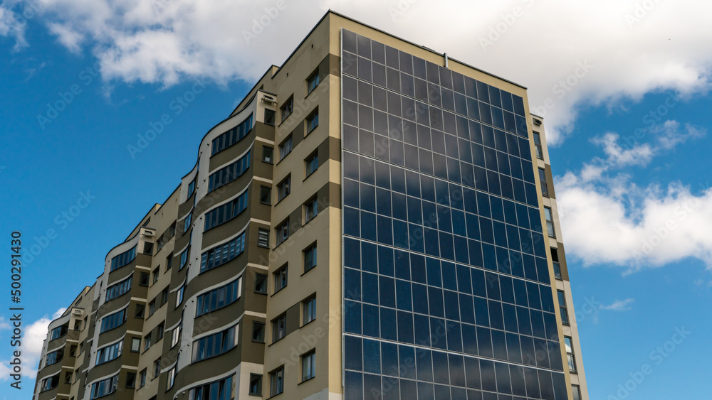 Movement of clouds against the background of a modern energy-efficient building. Multi-storey residential building with solar panels on the wall. Renewable energy in the city