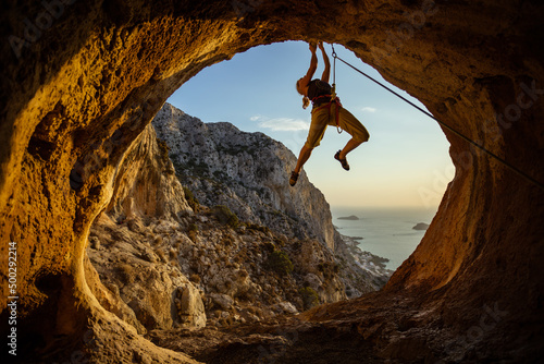 Young woman climbing challenging route in cave with beautiful sea view in background