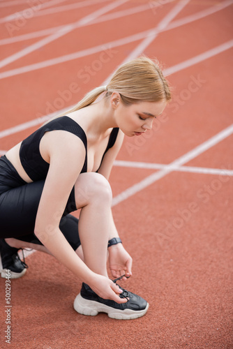 young blonde woman lacing sneaker on stadium. © LIGHTFIELD STUDIOS