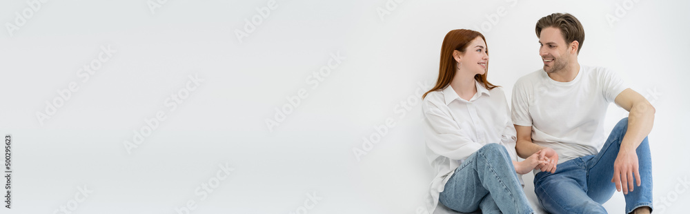 Positive young couple holding hands while sitting on white background, banner. Positive young couple holding hands while sitting on white background, banner.