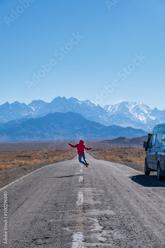 Boy or girl jumping in the middle of the road with a campervan at the side. Overland travel by campervan is an excellent experience to enjoy with the family.