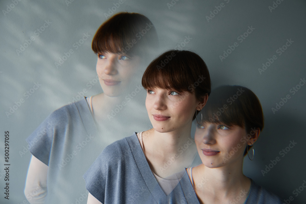 Repetitive exposure of dreamy young Caucasian woman with short hair standing against gray wall Repetitive exposure of dreamy young Caucasian woman with short hair standing against gray wall
