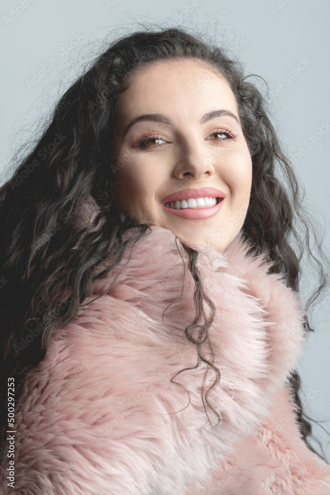 Beauty, fashion and make-up concept. Beautiful woman with long curly hair and fur pink coat studio portrait. Model with classic makeup and pink lipstick looking to camera with smile and white teeth Beauty, fashion and make-up concept. Beautiful woman with long curly hair and fur pink coat studio portrait. Model with classic makeup and pink lipstick looking to camera with smile and white teeth