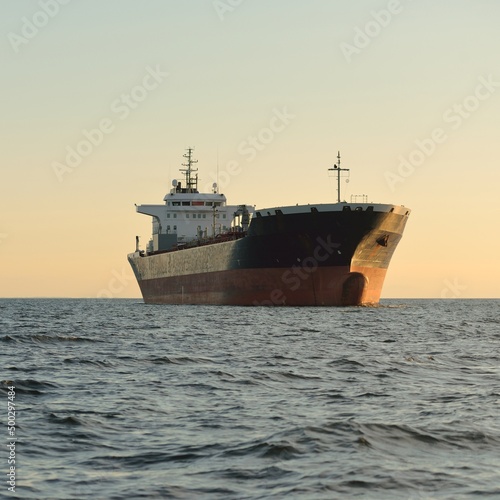 Large tanker ship sailing in an open sea at sunset. Golden sunlight. Freight transportation, fuel and power generation, nautical vessel, logistics, global communications, economy, business, industry