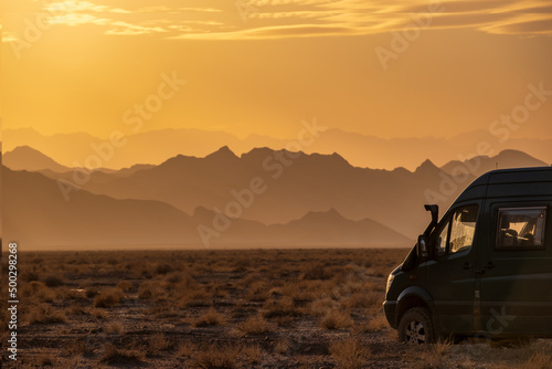 Rugged reliefs of the mountains in the Iranian desert at sunset with a 4x4 camper van on the side