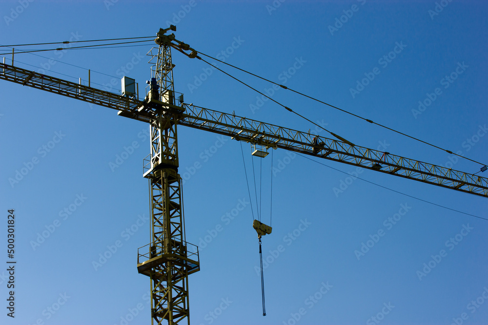 Construction crane against blue sky view from below. Construction site. Tower crane or slewing crane. Construction business concept. Building modern houses. Engineering lifting equipment. Real estate. Construction crane against blue sky view from below. Construction site. Tower crane or slewing crane. Construction business concept. Building modern houses. Engineering lifting equipment. Real estate.