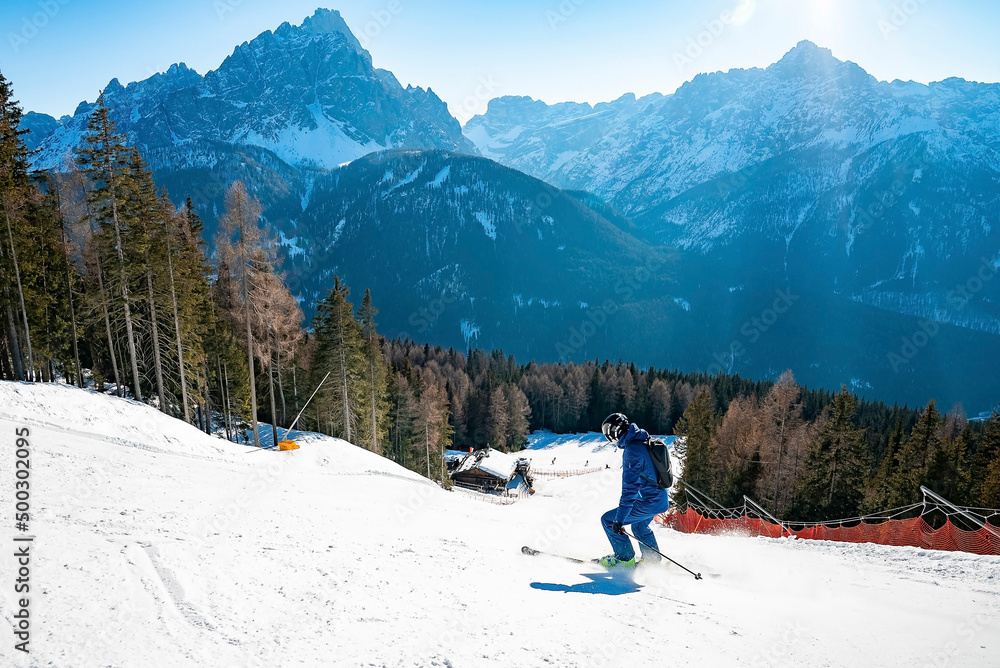 Skier skiing on snow covered downhill. Beautiful mountain range against blue sky. Tourist performing adventure sport during winter.