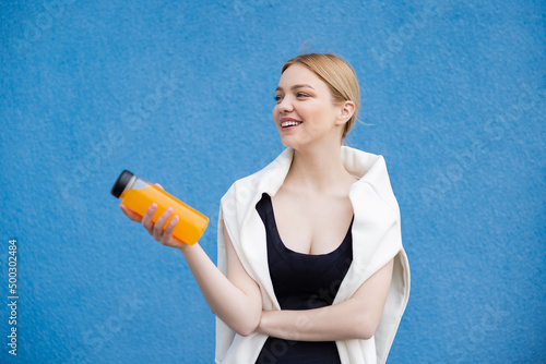 cheerful woman in sportswear holding orange juice on blue textured background.