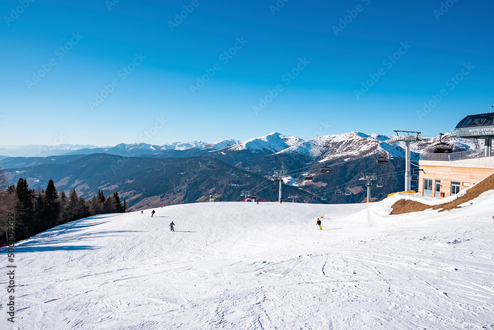 Scenic view of tracks by ski station on snowy landscape. Majestic mountains against clear blue sky. Idyllic view of alpine region during sunny day in winter.