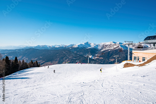 Scenic view of tracks by ski station on snowy landscape. Majestic mountains against clear blue sky. Idyllic view of alpine region during sunny day in winter.