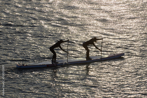 Silhouettes of two woman rowing with Stand up paddle SUP Dragon boards at evening river