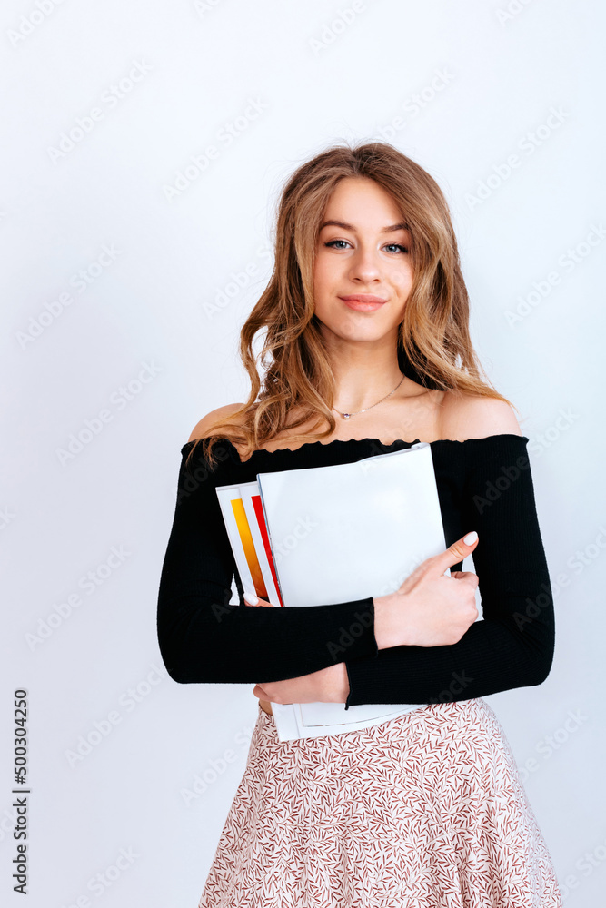 A student girl with long curly hair in a black blouse and skirt holds papers and educational materials. Papers without inscriptions in the hands of a girl.Copy space.