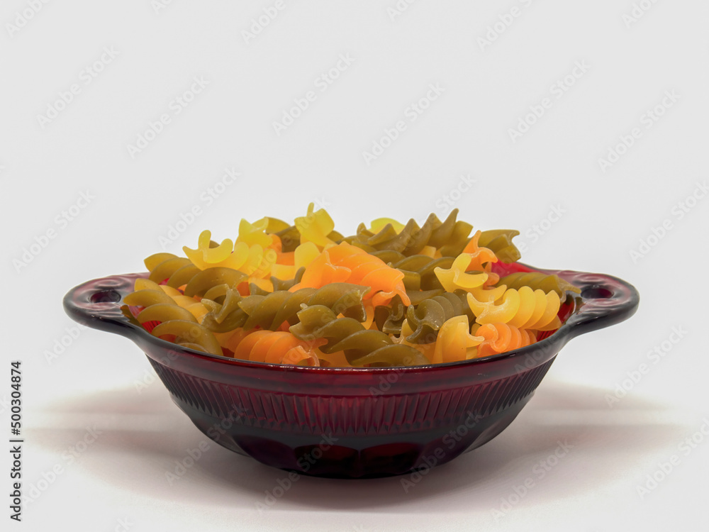 Studio shot of a heap of colorful raw fusilli pasta on a red glass plate against neutral background Studio shot of a heap of colorful raw fusilli pasta on a red glass plate against neutral background