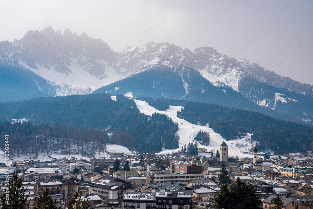 Beautiful view of crowded houses in village. Scenic townscape surrounded by majestic snowy mountain range. Holiday homes in south tyrol against sky during winter.
