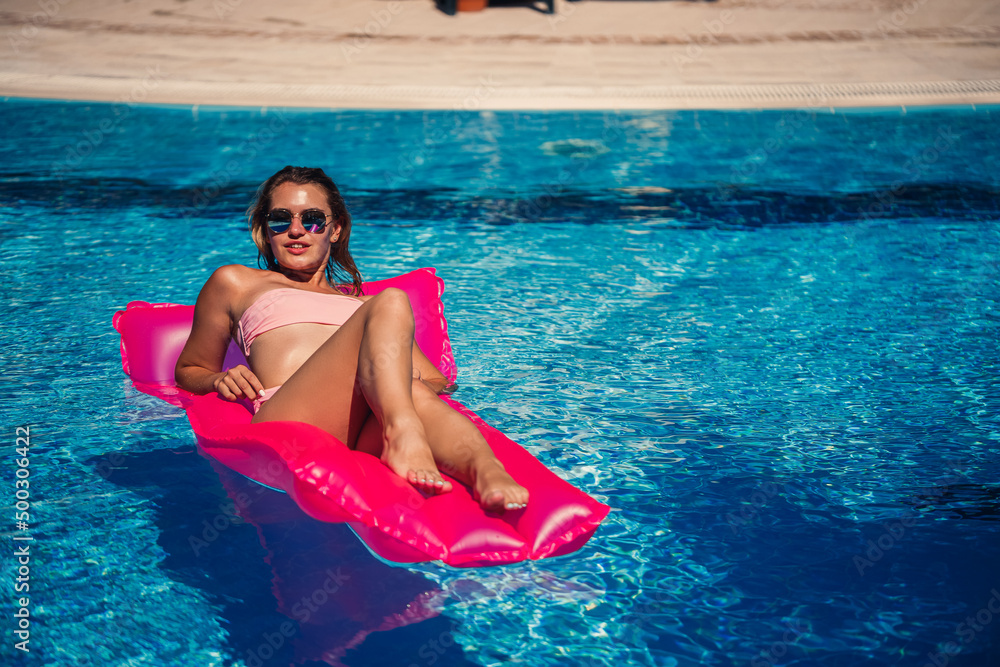 Sexy female model resting and sunbathing on a mattress in the pool. Woman in a pink bikini swimsuit floating on an inflatable pink mattress. spf and sunscreen
