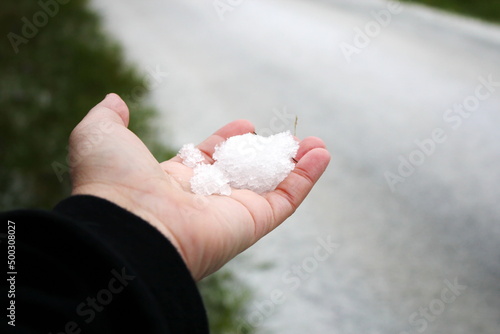 A man's hand holding snow in his hand after it snows against a snow-covered road in the background.