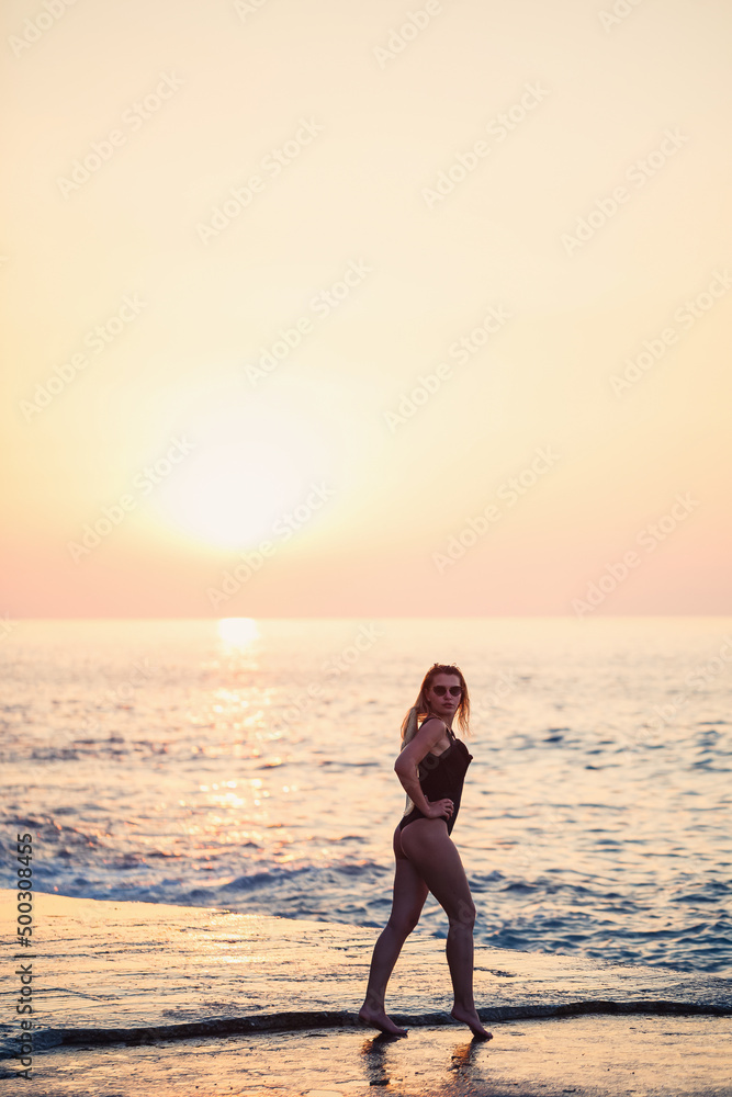 Beautiful lady in a black swimsuit on the seashore, Smiling face, with a straw hat on her shoulders. Golden sunset light