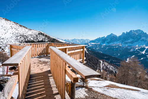 Viewing terrace over majestic mountains. Wooden observation point on top of snow covered range against clear blue sky. Scenic view in alps during winter. photo