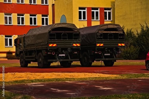 Wojskowe ciężarówki terenowe ( of road ) polskiej produkcji parkujące przodem do budynku dawnej szkoły .