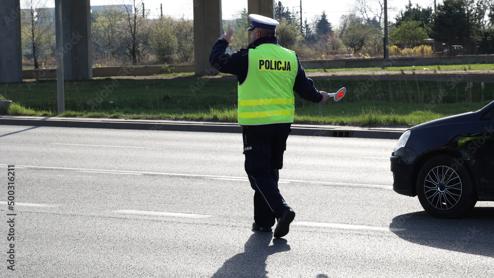  Policjant policji drogowej podczas kierowania ruchem z lizakiem do zatrzymywania pojazdów. - obrazy, fototapety, plakaty 
