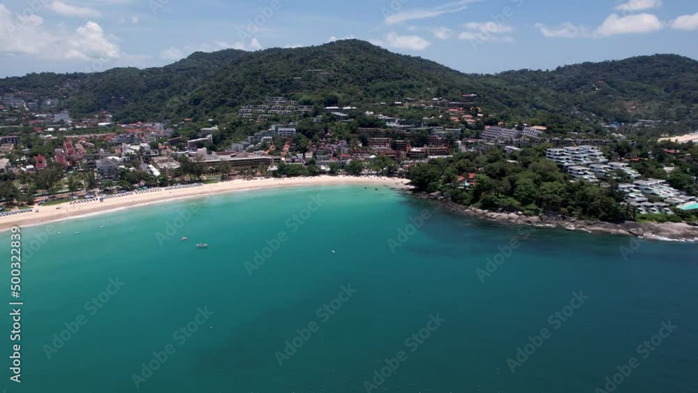 The snow-white Kata beach of Phuket island. Top view from a drone on the ocean waves. There are several Thai boats. The whole island is green. The water is clear and transparent. People are bathing The snow-white Kata beach of Phuket island. Top view from a drone on the ocean waves. There are several Thai boats. The whole island is green. The water is clear and transparent. People are bathing