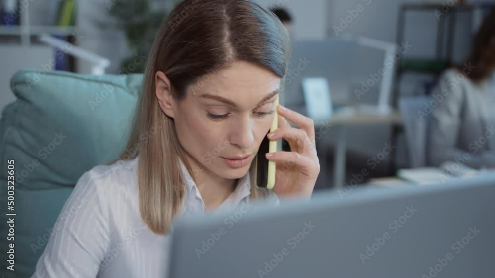 Close-up shooting of good-looking businesswoman in formal clothes talking on phone in modern office. Portrait of serious woman calling, sitting in front of computer in office interior. Ordinary Close-up shooting of good-looking businesswoman in formal clothes talking on phone in modern office. Portrait of serious woman calling, sitting in front of computer in office interior. Ordinary