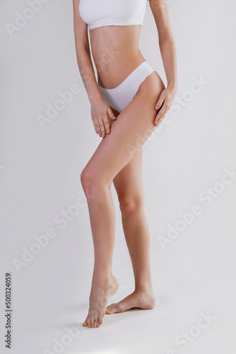 Cropped shot of lower half of slim female's body in white underwear. Unrecognizable fit woman in lingerie posing over isolated white background. Copy space for text, close up.