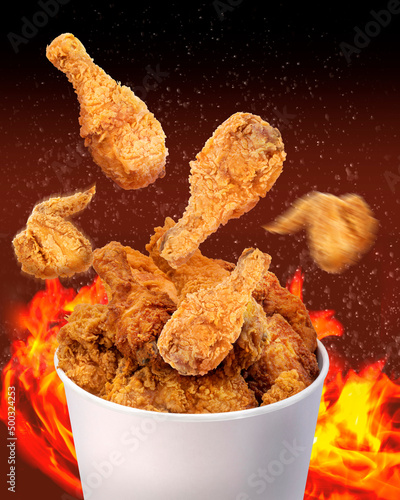 Fried chicken flying out of paper bucket over hot flame background, Hot and spicy Fried chicken on black and red background.