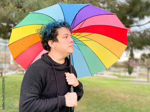 Photos A smiling young woman poses with an open rainbow umbrella in a park