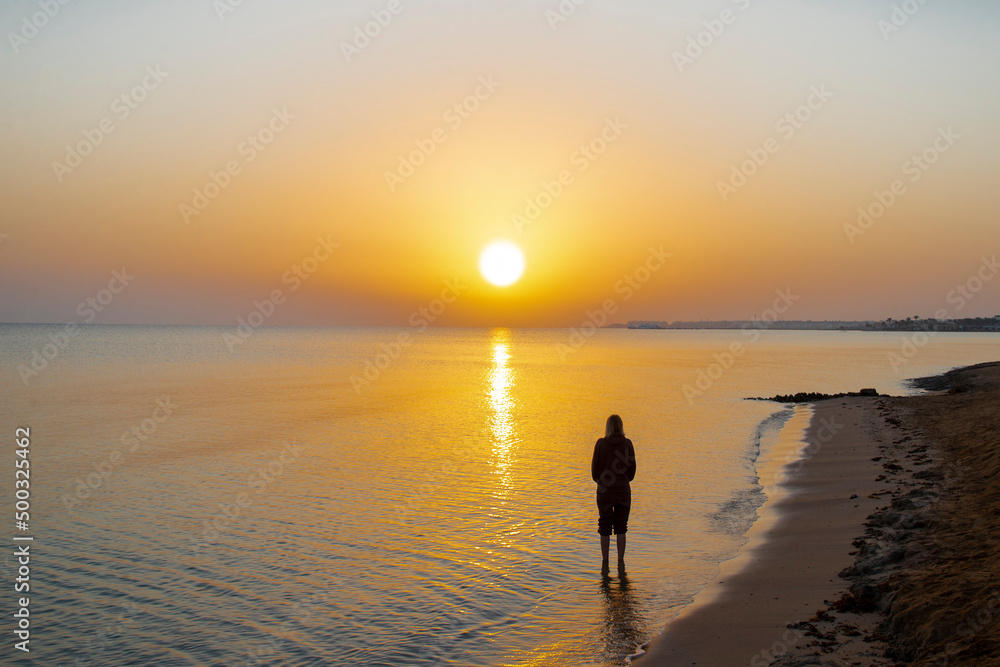 Silhouette of woman looking at a landscape of sunrise, sun, sky and beach on the shores of the Red Sea in Hurgada, Egypt