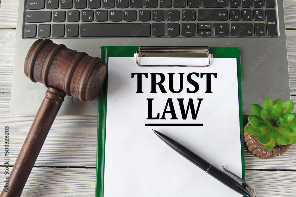 TRUST LAW - words on a white sheet on the background of a laptop, a court hammer and a pen