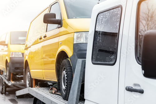 White small cargo truck car carrier loaded with two yellow van minibus on flatbed platform and semi trailer tow on roadside highway road. Volunteer support delivery transport for ukrainina people