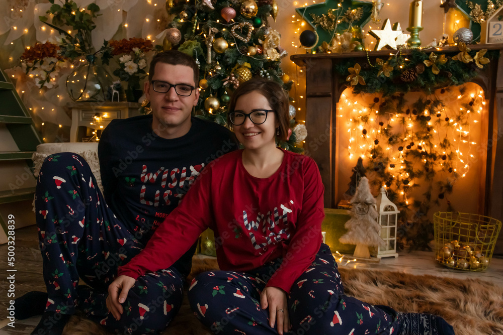 a girl and a guy are sitting on the floor near the Christmas tree and fireplace 